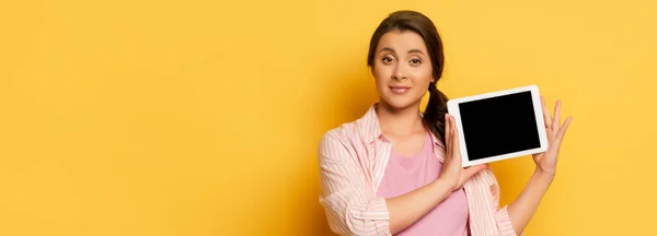 Horizontal image of young woman showing digital tablet with blank screen on yellow — Stock Photo