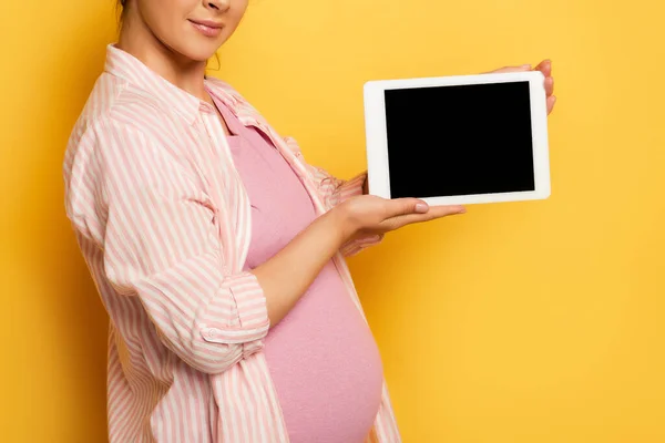Обрізаний вид вагітної жінки, що показує цифровий планшет з порожнім екраном на жовтому — стокове фото