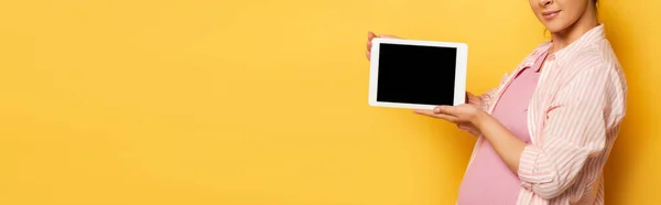 Vue recadrée de la jeune femme enceinte tenant tablette numérique avec écran blanc sur jaune, image horizontale — Photo de stock