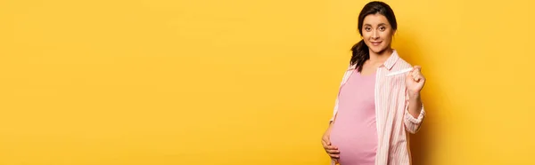 Website header of pregnant woman touching belly and showing pregnancy test on yellow, horizontal image — Stock Photo