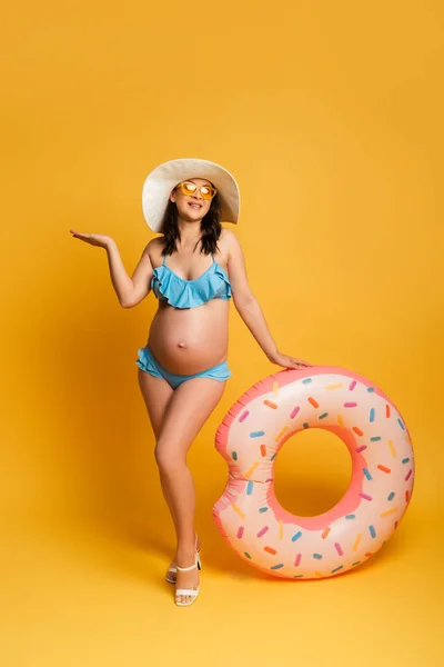 Vue pleine longueur de la femme enceinte avec anneau de natation posant sur jaune — Photo de stock