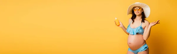 Immagine orizzontale della donna incinta in costume da bagno con crema solare su giallo — Foto stock