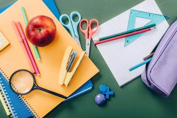 Draufsicht auf ganze Äpfel und Notizbücher in der Nähe von Schulschreibwaren auf grüner Tafel — Stockfoto