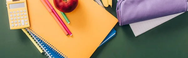 Top view of multicolored notebooks and school supplies on green chalkboard, horizontal image — Stock Photo