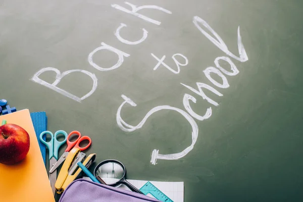 Selective focus of school supplies and fresh apple near back to school lettering on green chalkboard — Stock Photo