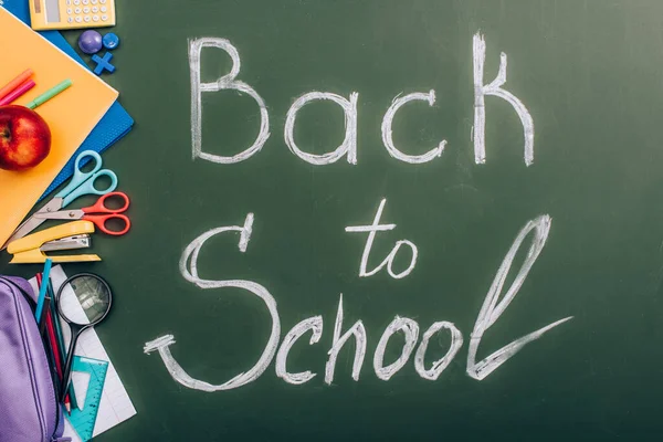 Top view of back to school inscription near school supplies and fresh apple on green chalkboard — Stock Photo