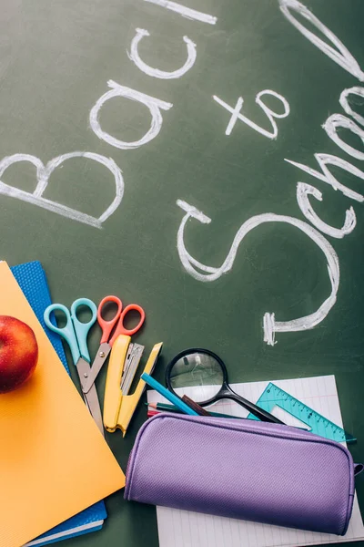 Selective focus of back to school lettering near school stationery and fresh apple on green chalkboard — Stock Photo