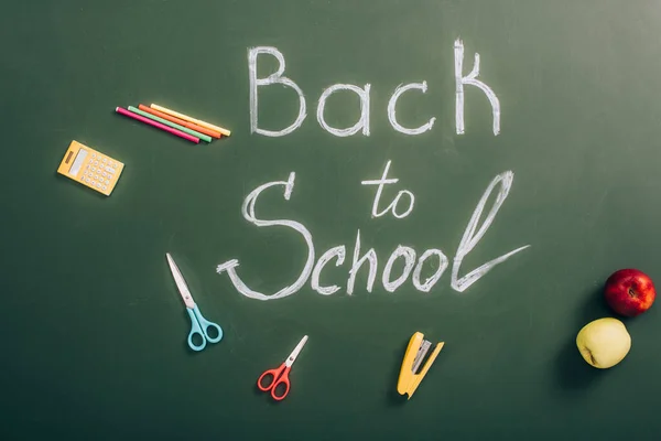 Top view of back to school lettering near school supplies and ripe apples on green chalkboard — Stock Photo