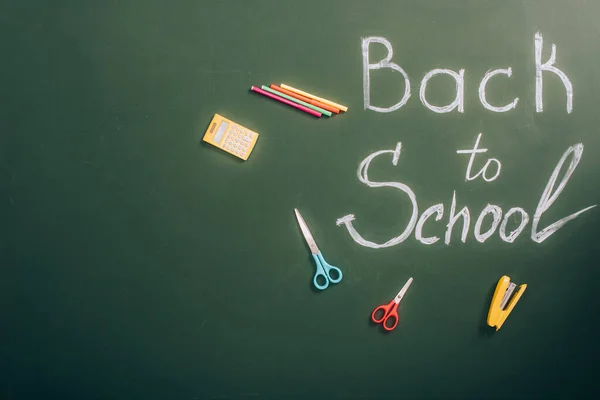 Top view of back to school inscription near school stationery on green chalkboard with copy space — Stock Photo