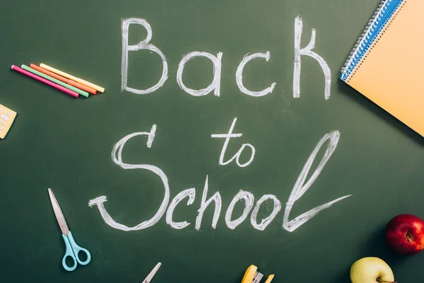 Vue du dessus du lettrage de retour à l'école près des pommes et des fournitures scolaires sur un tableau vert — Photo de stock