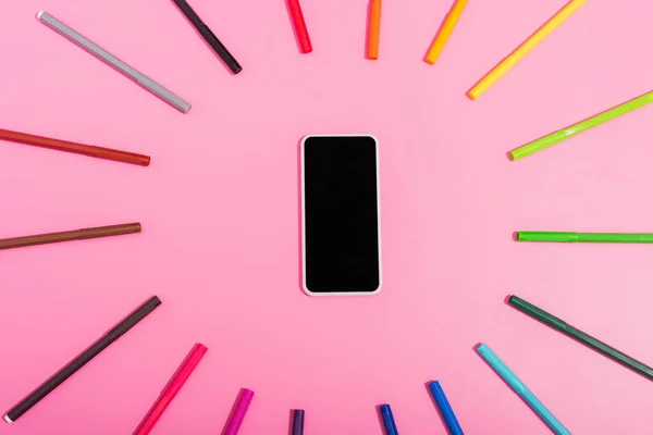 Top view of smartphone with blank screen framed by color felt tip pens on pink — Stock Photo