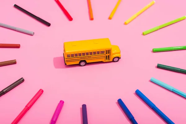 Vista de ángulo alto del modelo de autobús escolar en marco de plumas de fieltro multicolores en rosa - foto de stock