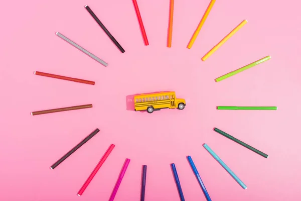 Top view of school bus model framed by color felt pens on pink — Stock Photo