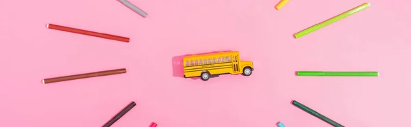 Ansicht des Schulbusmodells von oben eingerahmt mit Farbfilzstiften auf rosa, horizontalem Bild — Stockfoto