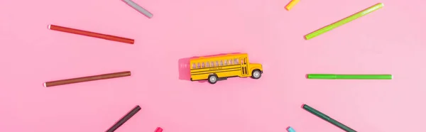 Top view of school bus model framed with color felt tip pens on pink, horizontal image — Stock Photo