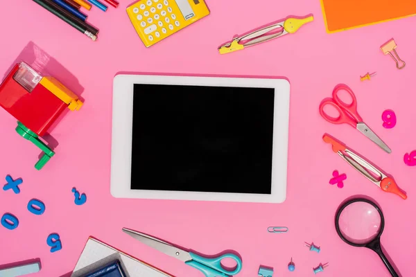 Вид сверху на цифровой планшет с пустым экраном рядом со школьной канцелярской принадлежностью на розовом — стоковое фото