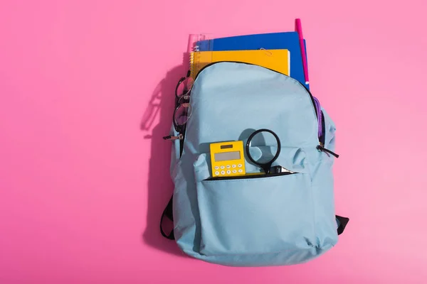 Vista superior da mochila azul com cadernos, calculadora, óculos e material escolar em rosa — Fotografia de Stock