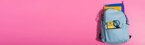 Draufsicht auf blauen Rucksack voller Schulbedarf auf rosa mit Kopierraum, horizontales Bild — Stockfoto