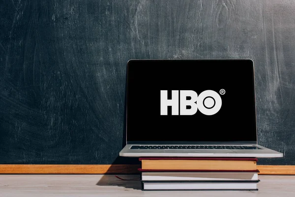 KYIV, UCRANIA - 7 de julio de 2020: Computadora portátil con sitio web de HBO en la pila de libros cerca de pizarra negra - foto de stock