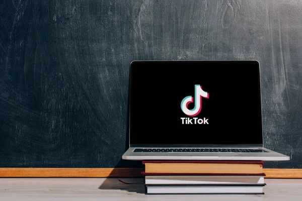 KYIV, UCRANIA - 7 de julio de 2020: Ordenador portátil con el sitio web Tik Tok en libros apilados cerca de pizarra negra - foto de stock