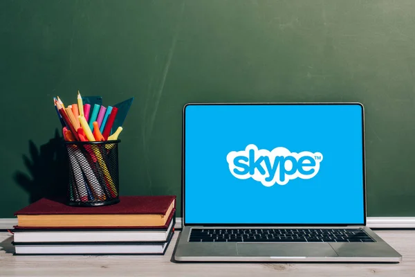 KYIV, UCRAINA - 7 LUGLIO 2020: Portatile con sito web Skype vicino al portapenne con cancelleria su libri di testo impilati vicino alla lavagna verde — Foto stock