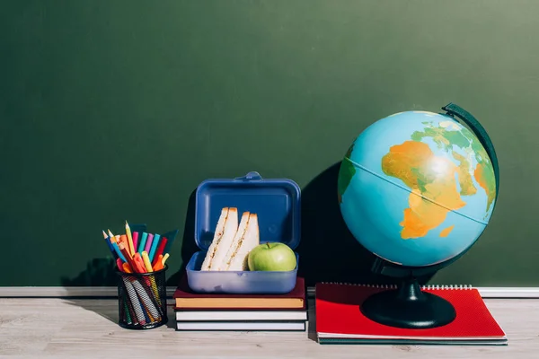 Globe near lunch box on books and pen holder near green chalkboard — Stock Photo