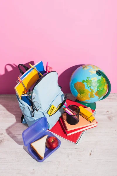 Vista de alto ângulo da mochila com material escolar perto do globo, lancheira, papelaria e modelo de ônibus escolar em rosa — Fotografia de Stock