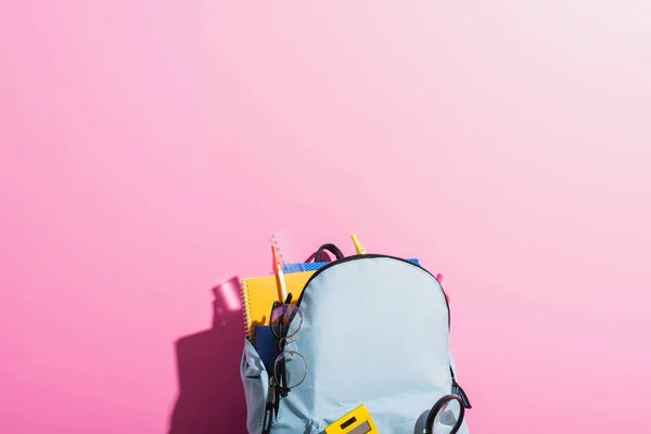 Blue backpack with school stationery and eyeglasses on pink — Stock Photo