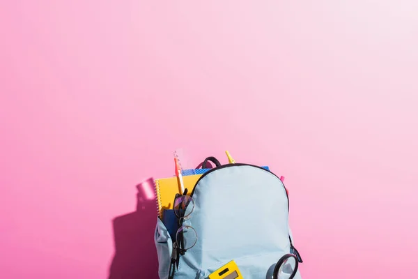 Mochila azul con papelería escolar y anteojos en rosa - foto de stock