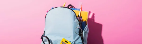 Horizontal image of blue backpack with school supplies and eyeglasses on pink — Stock Photo