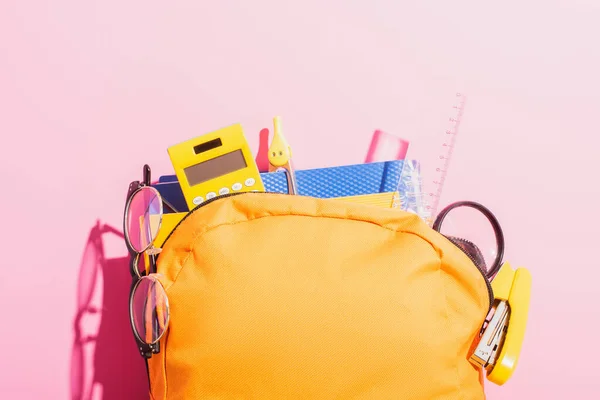 Zaino giallo imballato con materiale scolastico e occhiali su rosa — Foto stock