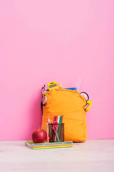 Mochila escolar embalada perto de cadernos, suporte de caneta com artigos de papelaria e maçã madura em rosa — Fotografia de Stock