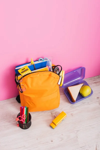High angle view of backpack with school supplies near school bus model, lunch box and pen holder with felt pens and scissors on pink — Stock Photo