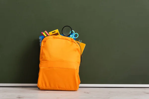 Mochila amarilla llena de papelería escolar en el escritorio cerca de pizarra verde - foto de stock