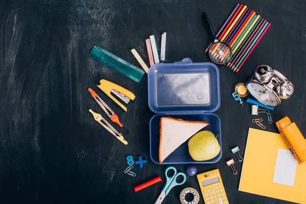 Vista superior da lancheira com maçã inteira e sanduíches saborosos perto de artigos de papelaria escolar em quadro-negro — Fotografia de Stock