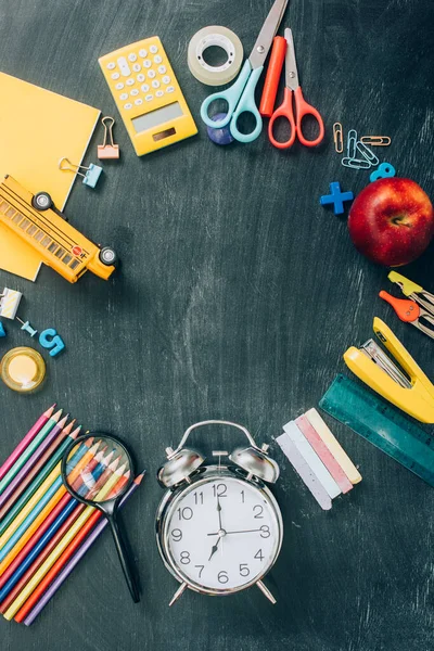 Vista superior del marco con manzana madura, modelo de autobús escolar, reloj despertador vintage y útiles escolares en pizarra negra - foto de stock