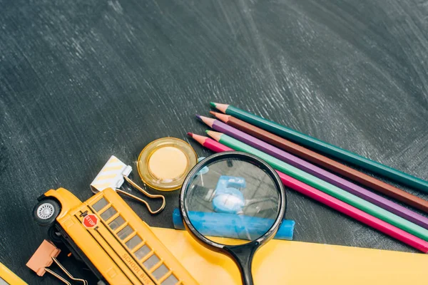 Top view of school bus model, magnifier and school supplies on black chalkboard — Stock Photo