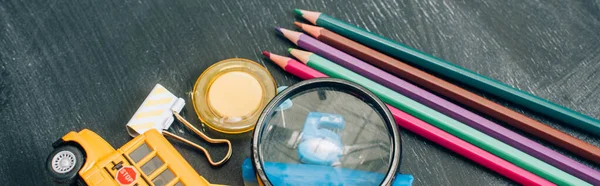 Vista de ángulo alto de lupa, lápices de color y útiles escolares en pizarra negra, plano panorámico - foto de stock