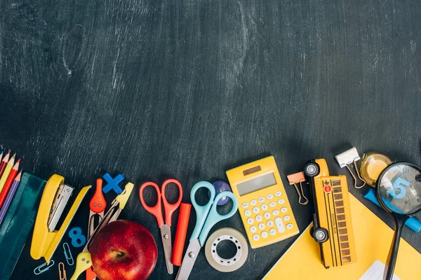 Top view of school bus model, ripe apple and school supplies on black chalkboard with copy space — Stock Photo