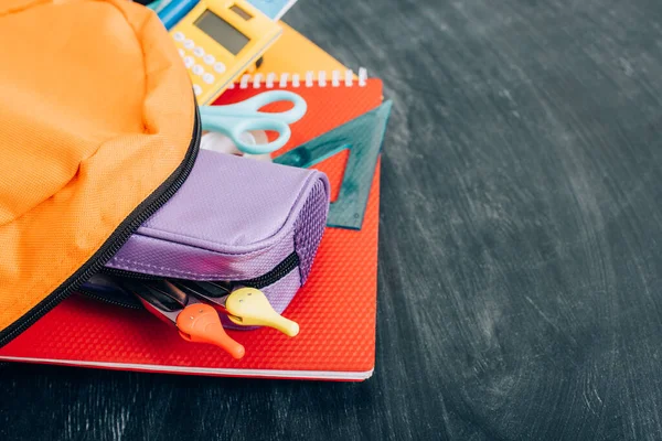 Mochila amarilla con papelería escolar multicolor en pizarra negra - foto de stock