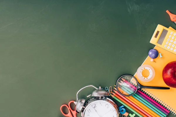 Top view of vintage alarm clock near school stationery on green chalkboard with copy space — Stock Photo