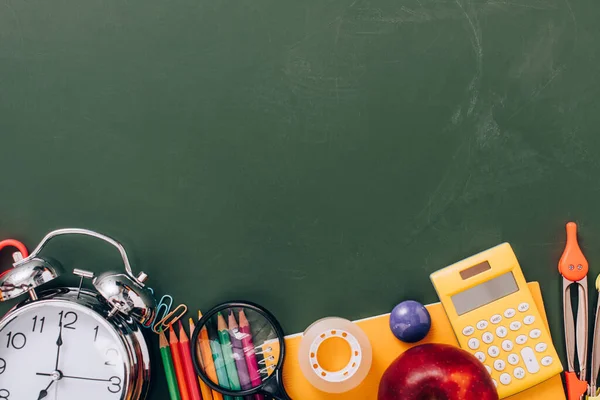 Top view of vintage alarm clock and ripe apple near school stationery on green chalkboard with copy space — Stock Photo