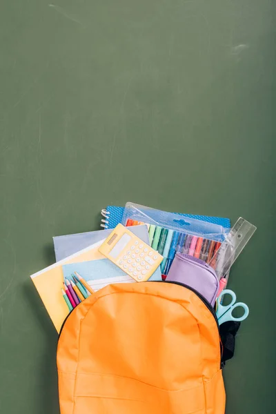 Vista dall'alto dello zaino pieno di cancelleria scolastica sulla lavagna verde — Foto stock