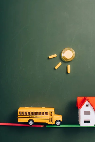 Верхний вид школьных автобусов и моделей домов на дороге из карандашей, и солнце из магнитов на зеленой доске — стоковое фото