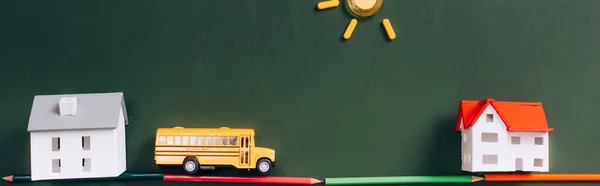 Top view of toy school bus and house models on road made of color pencils, and sun made of magnets on green chalkboard, horizontal image — Stock Photo