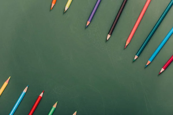 Rows of color pencils on green chalkboard, top view — Stock Photo