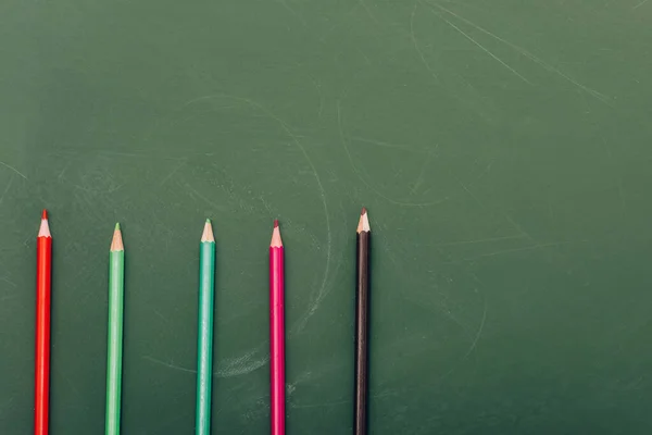 Top view of row of multicolored pencils on green chalkboard — Stock Photo