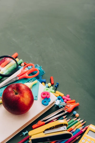 High angle view of apple on book near school stationery on green chalkboard — Stock Photo