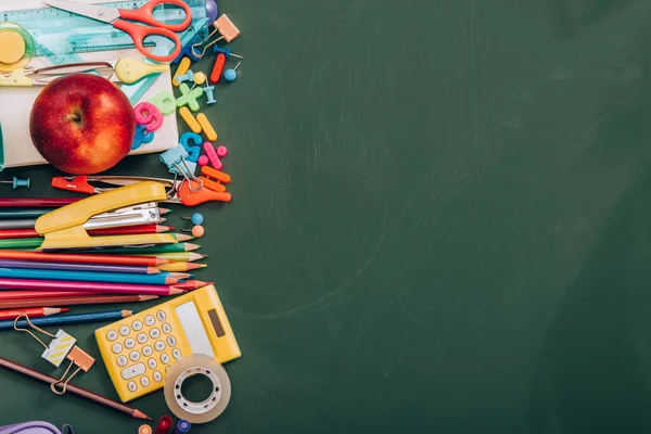 Top view of ripe apple, calculator and school stationery on green chalkboard with copy space — Stock Photo