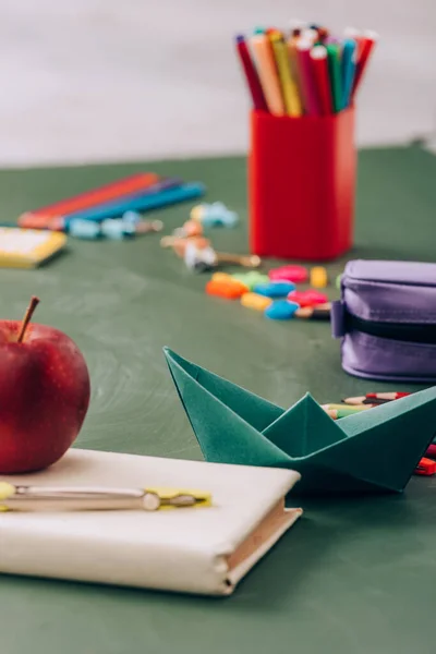 Selective focus of ripe apple and compass divider on book near school stationery on green chalkboard — Stock Photo